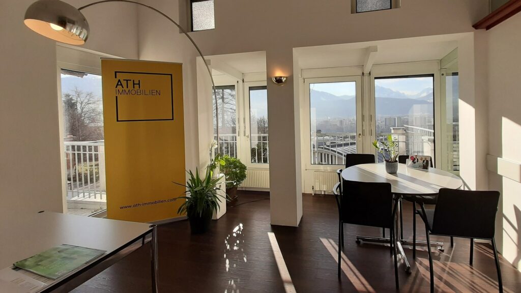 Unser Immobilienbüro in Innsbruck Arzl - Innenansicht mit Arbeitsplatz eines Immobilienmaklers und Rollup mit ATH Immobilien Logo