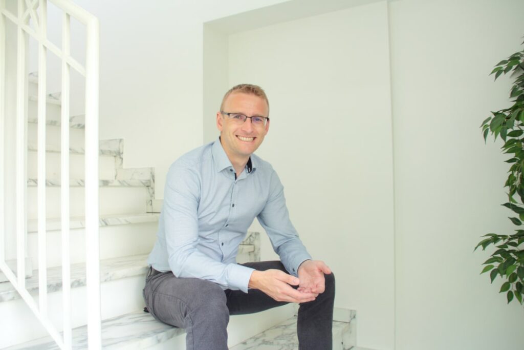 Kompetenter Immobilienmakler, Andreas Thaler von ATH Immobilien, sitzt in einem weißen Treppenhaus auf der Treppe